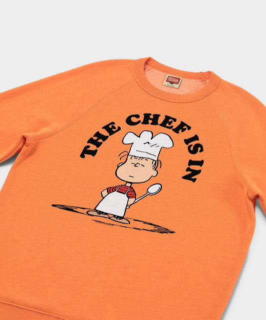Orange crewneck sweatshirt featuring Linus van Pelt with a chef hat and apron on the front-1