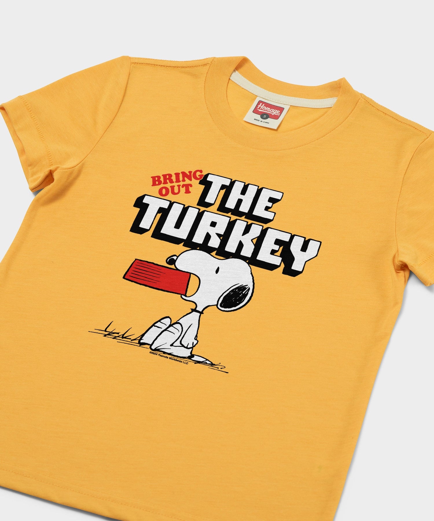Close-up of the front graphic showing Snoopy sitting happily with festive holiday elements on the gold fabric