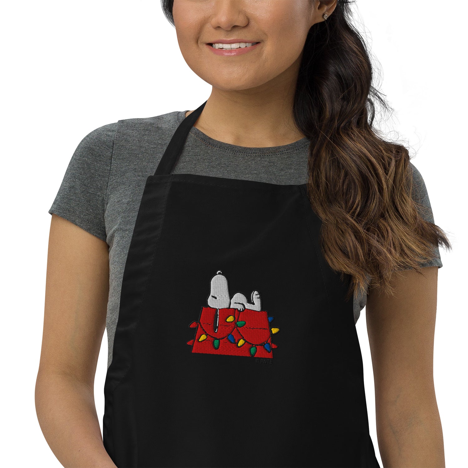 Close-up of the embroidered Snoopy on his doghouse design centered on the front of the apron